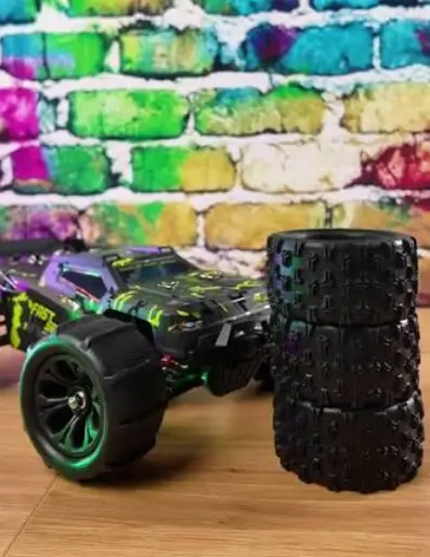 WIAORCHI Tenspeed RC truggy on paddle tyres parked next to a stack of spare tyres in front of a painted brick wall